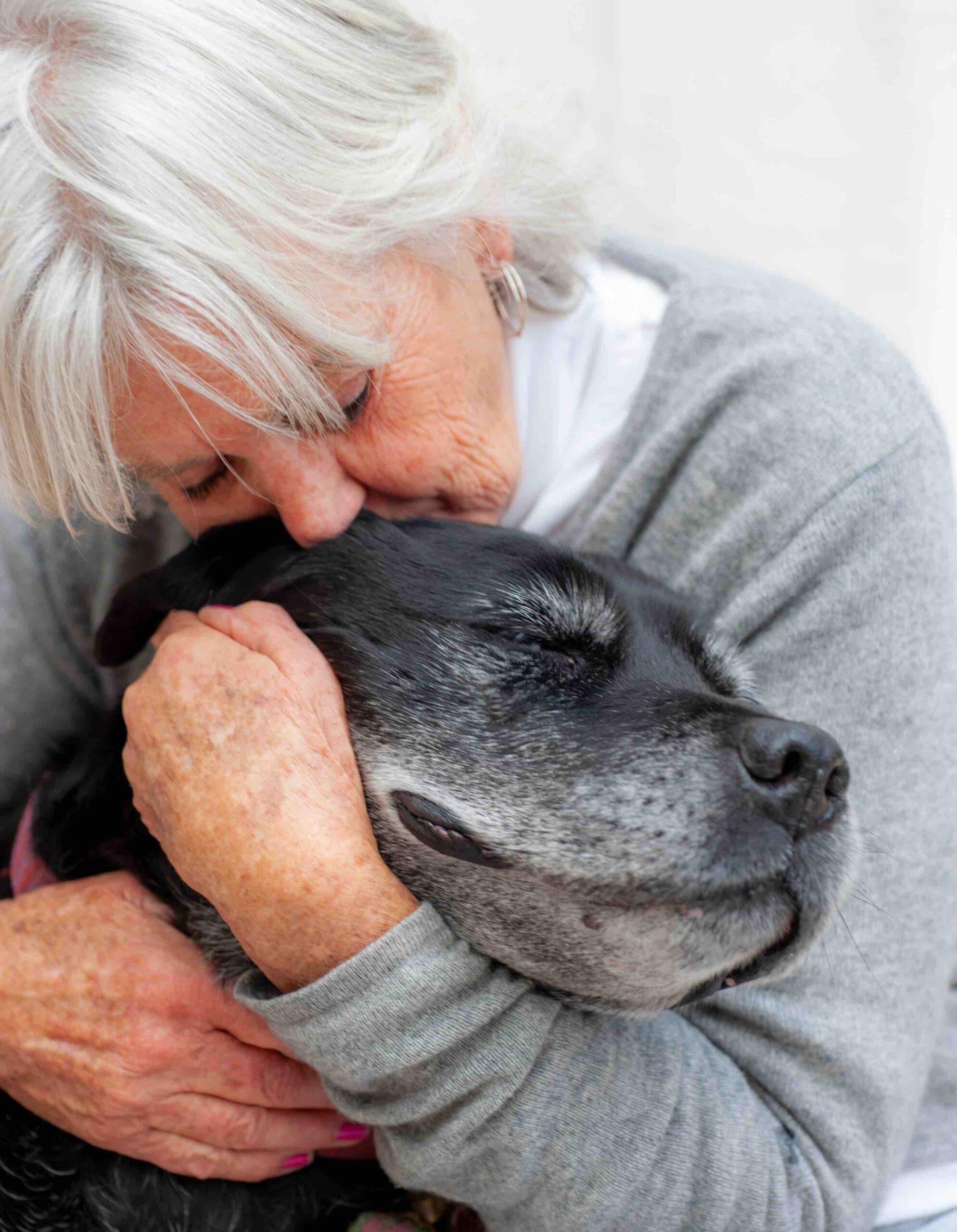 A senior woman gently embraces an elderly black dog, both at peace and safe—symbolizing mutual rescue through adoption from Humane Animal Rescue of Pittsburgh.